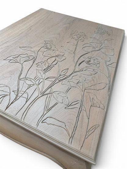 A close-up of a light natural wood top with engraved floral line art. 