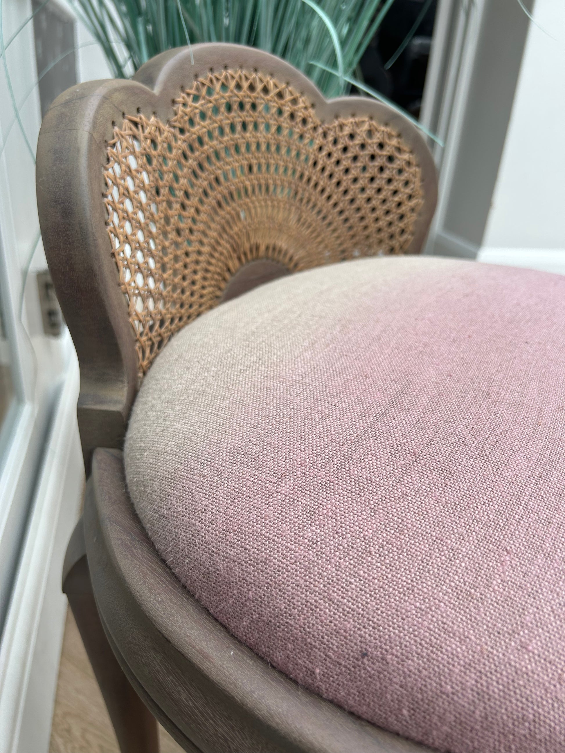 Close-up of a chair with woven cane backrest and cream to pink cushion